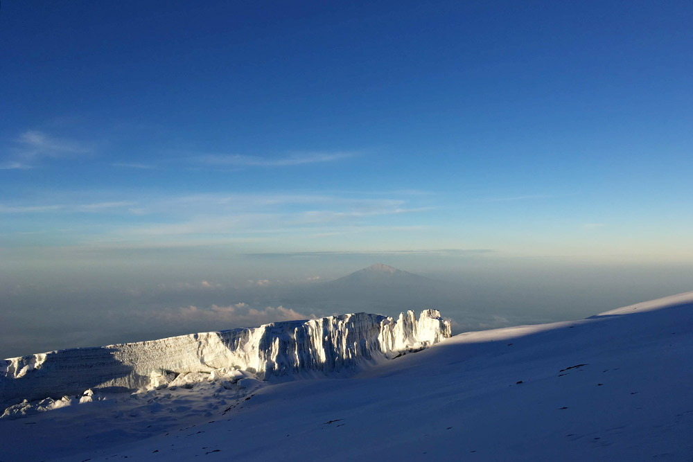 Вид с вершины Килиманджаро на ледники на склонах и пик Меру — вдалеке на заднем плане