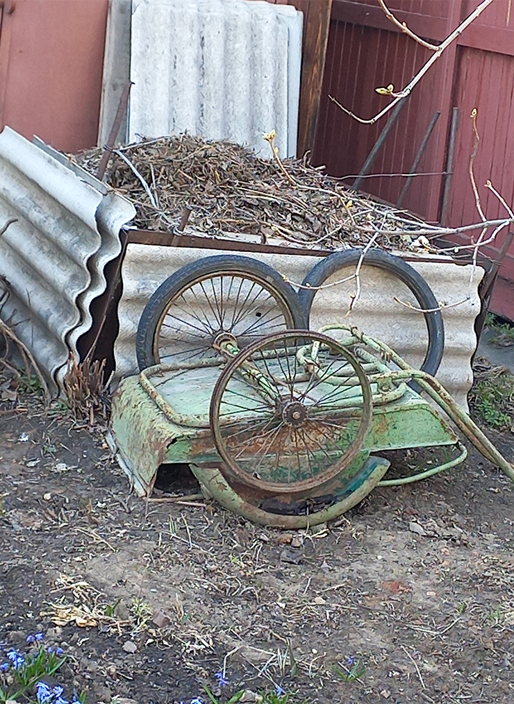 Этот компостер собран из старых листов железа. Их удерживают металлические трубки, вбитые в землю. Шифер здесь просто так прислонен, никакой роли он не играет. Тачка — ждет ремонта