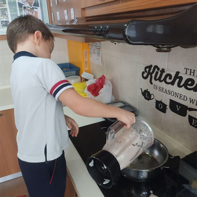 Сын готовит оладьи на кухне садика