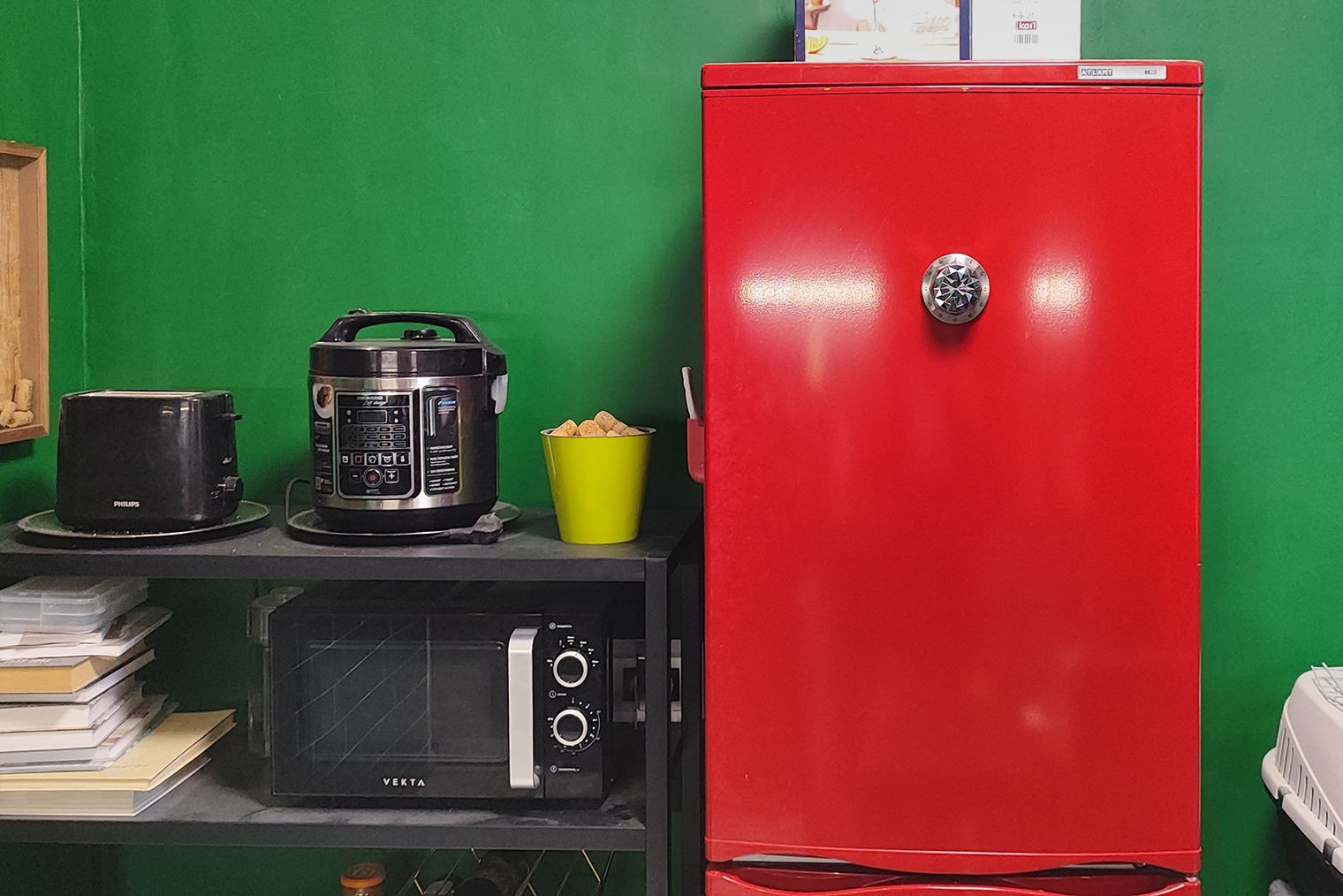 Это черный стеллаж из «Икеи», а рядом с ним — холодильник «Атлант»