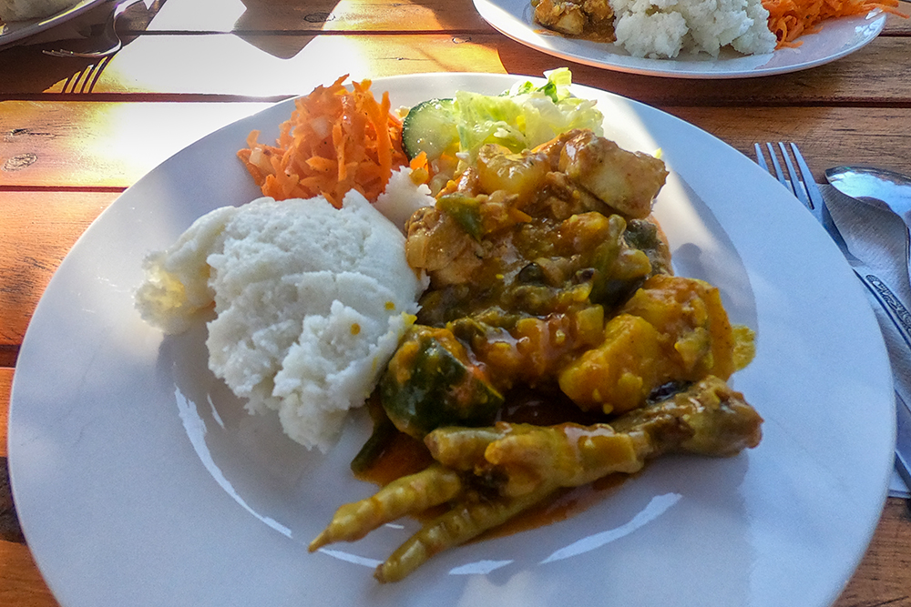 Пробуем африканскую еду в тауншипе Соуэто. На тарелке куриное мясо с лапкой, тот самый рис⁠-⁠манка и салат из капусты, огурцов и моркови