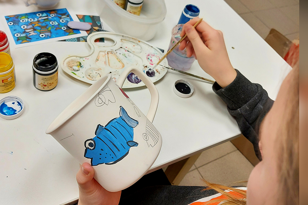 Дети рисуют на фарфоровых заготовках красками в подглазурной технике. После этого мы еще раз обожжем кружку, чтобы ее можно было мыть и не бояться за рисунок