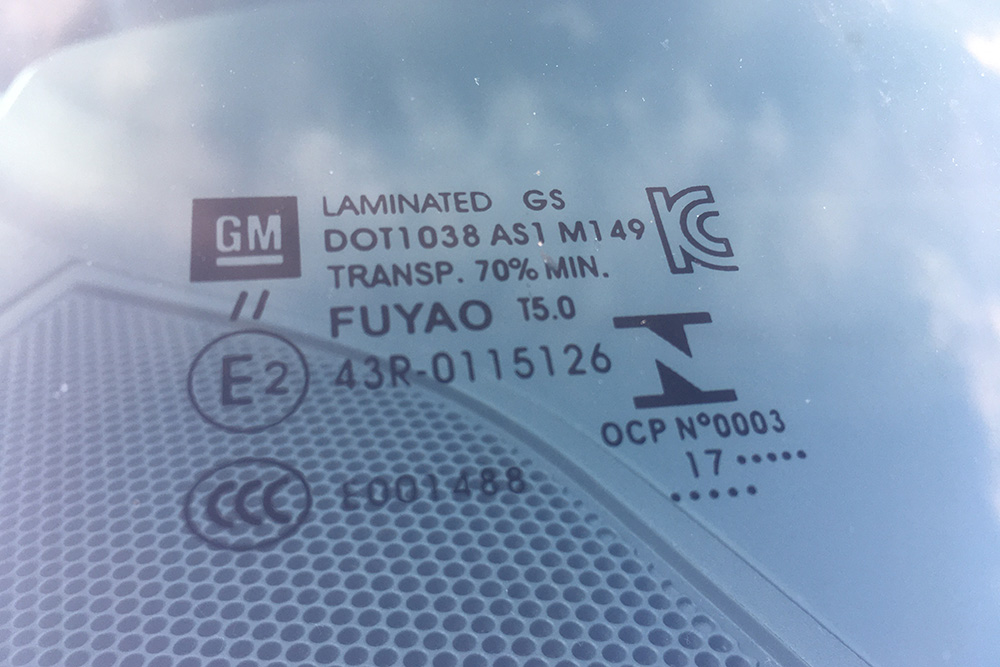 На стекле есть данные о сертификации, значок производителя автомобиля. В этом случае — «Дженерал Моторс». Цифра 17 в нижней строчке — год производства стекла. Иногда пишут только последнюю цифру
