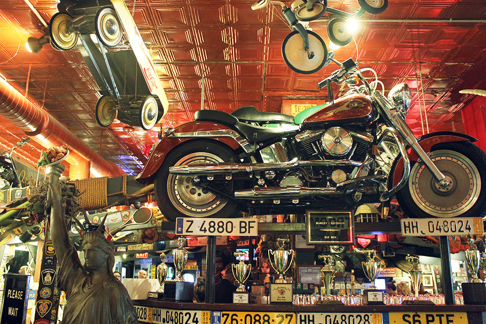 Интерьер бара напоминает музей: всюду мотоциклы и машины, автомобильные номера, значки и трофеи. К факелу статуи Свободы прилепили тарелку с куриными крылышками — это тоже символ Америки