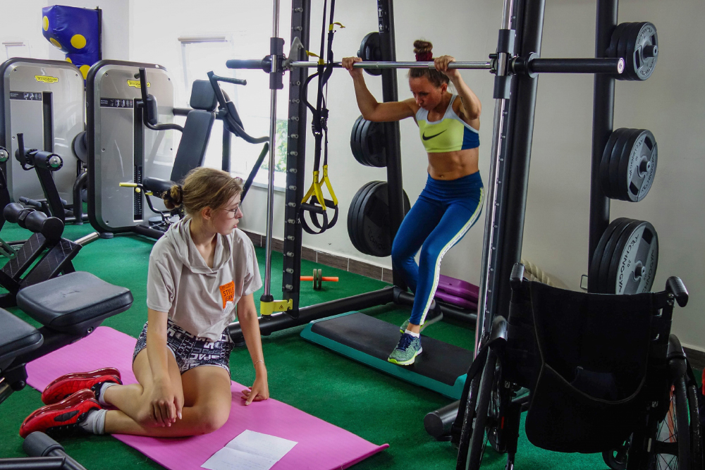 На тренажере — тренер по адаптивной физкультуре Ольга Полыгалова с несовершенным остеогенезом первого типа. Помимо тренерской работы она занимается тяжелой атлетикой
