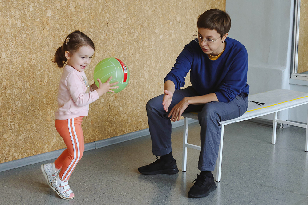 В этом упражнении Варя учится играть в мяч. Она бросает его в стену и старается поймать. Для нее это тренировка баланса и быстрого скоординированного движения. Также этот навык важен, чтобы участвовать в совместных играх с другими детьми. Автор фото: Аглая Владимирова