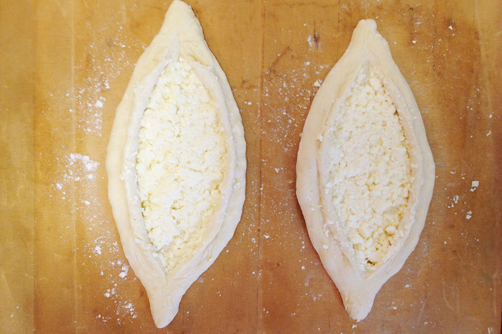 Из аккуратно отогнутых краев выглядывает сыр. Существуют разные способы формовки хачапури по⁠-⁠аджарски, но именно этот, на мой взгляд, позволяет показать всю красоту выпечки