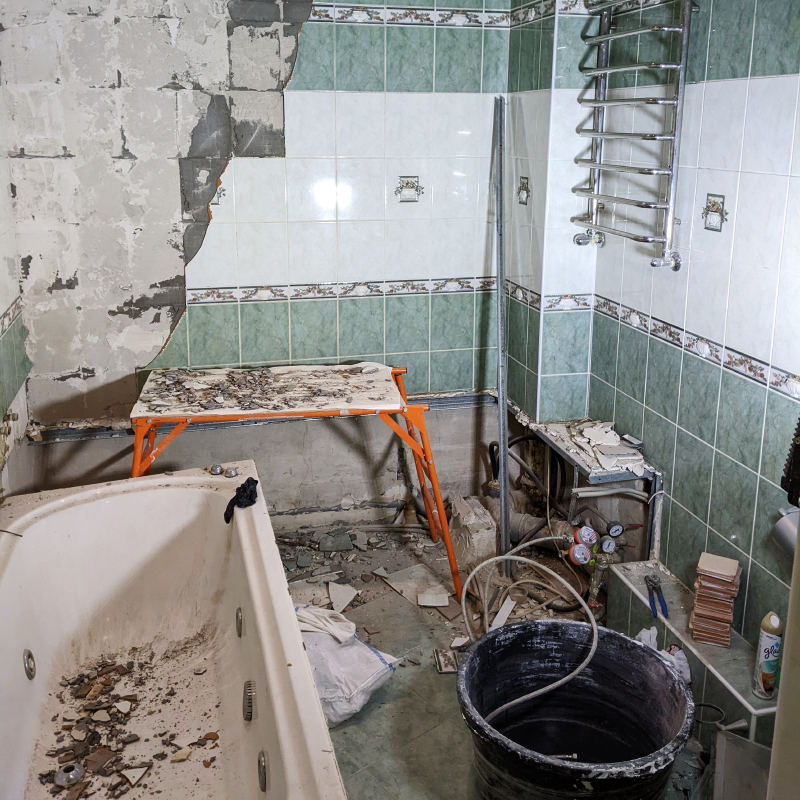 Фото отлично передает процесс: часть плиток уже сбита, ванна снята, потолок демонтирован, но в то же время часть комнаты еще цела