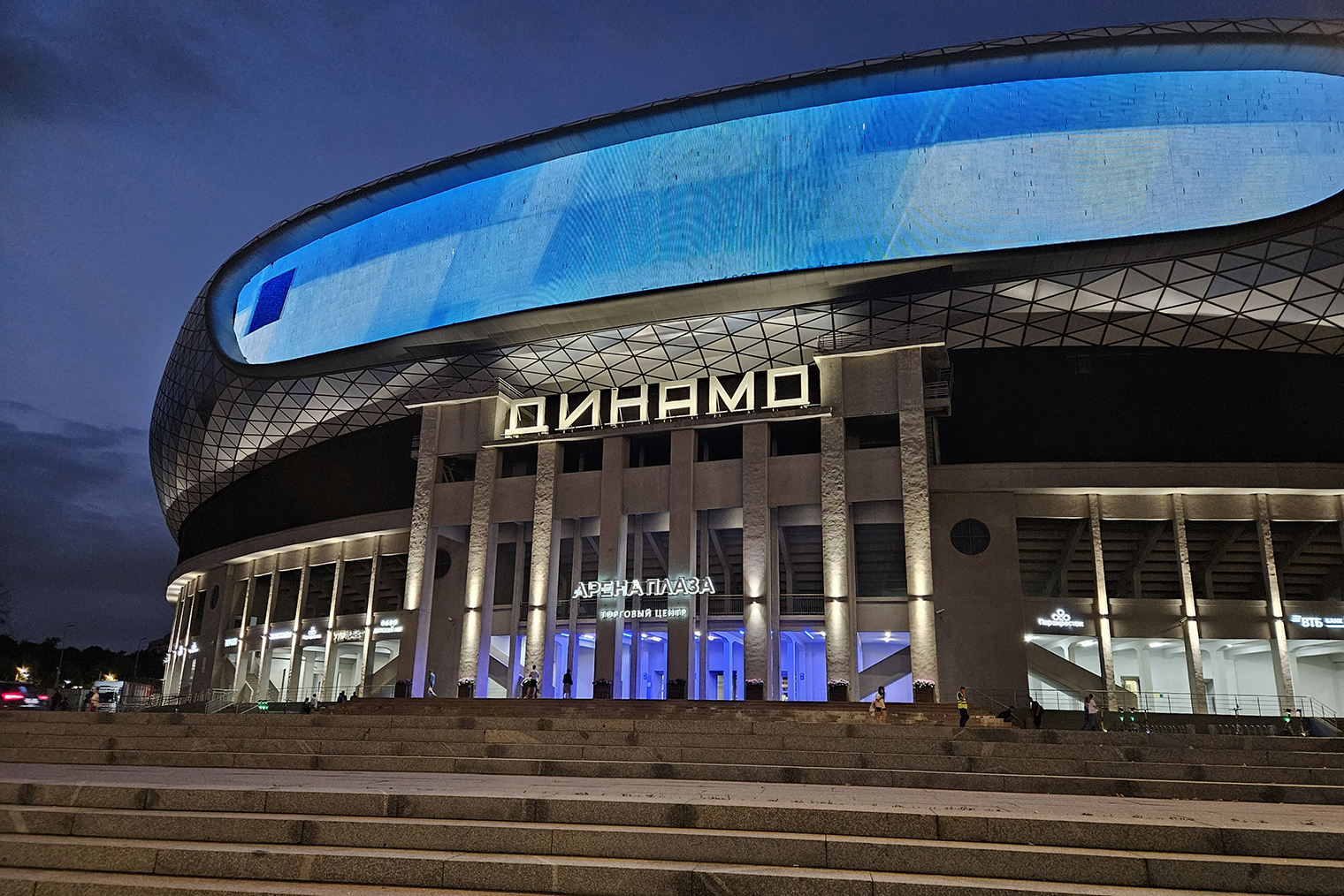 Фото стадиона «Динамо» на Galaxy Z Fold 5 смотрится неплохо, но зернистые шумы в тенях и пересвеченные белые вывески портят впечатление. Зато синее освещение на входе передано точно