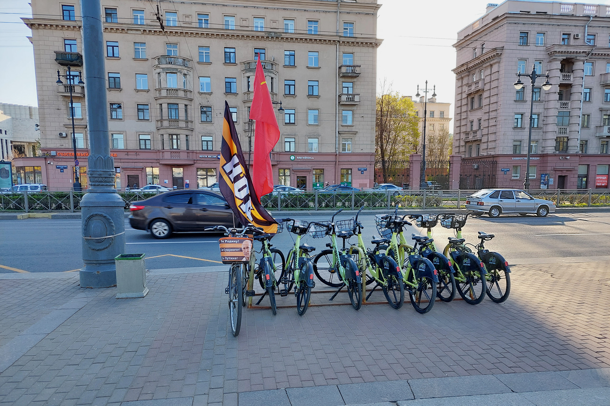 Велосипеды Smartbike у метро «Парк Победы». К парковке кто⁠-⁠то прицепил свой велосипед с флагами