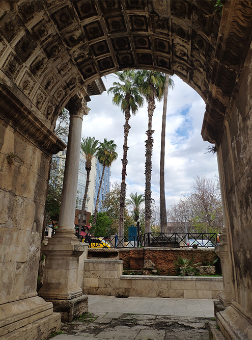 В арке виден современный район Антальи. На его фоне древние ворота выглядят необычно