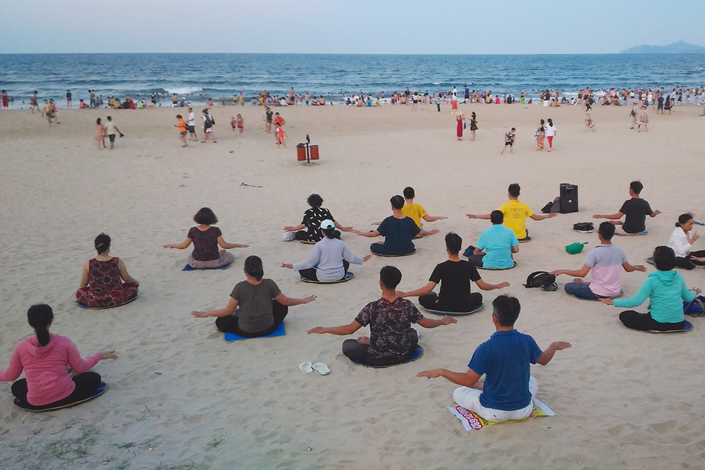 Вьетнамцы на закате занимаются йогой на пляже, это бесплатная группа для всех желающих